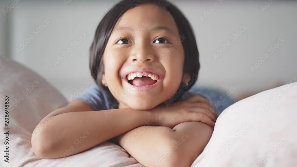 Cheerful toothless little girl watching TV while laughing and lying in the bedroom at home. Shot in 4k resolution Cheerful toothless little girl watching TV while laughing and lying in the bedroom at home. Shot in 4k resolution
