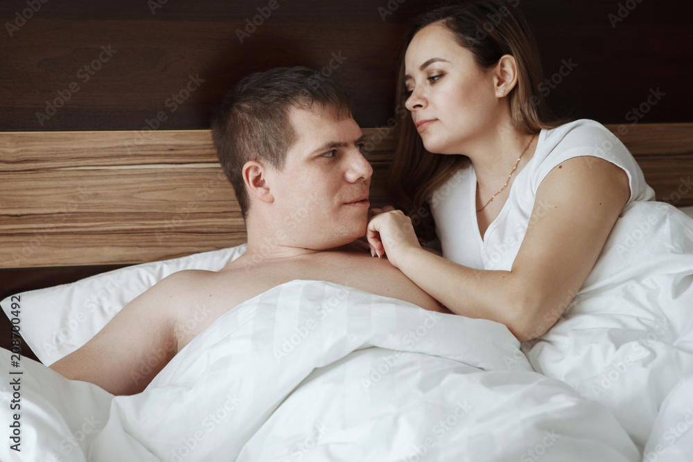 Young beautiful husband and wife resting in bed under a white blanket in a hotel room Young beautiful husband and wife resting in bed under a white blanket in a hotel room