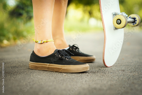 view of the legs of a girl with a skateboard on the street on a summer day