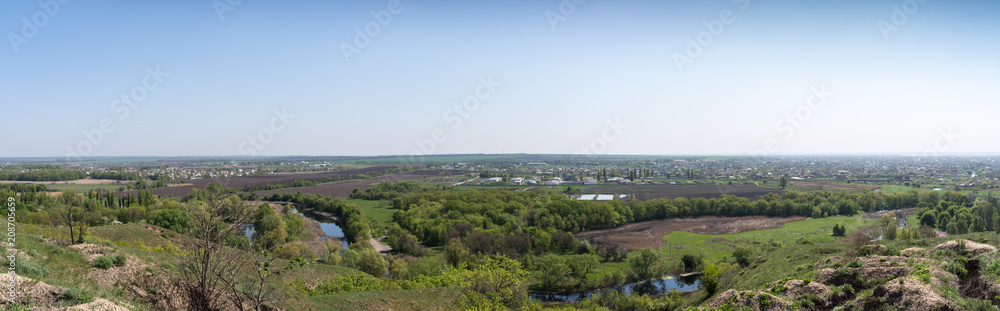 Panorama. View from the hill to the lake, fields and a small town