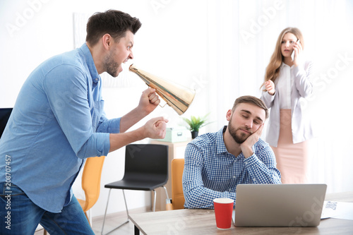 Angry boss with megaphone screaming at sleeping employee in office