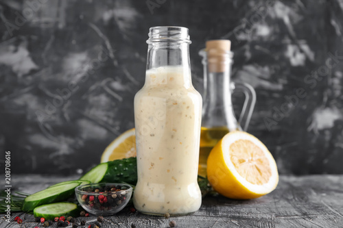 Bottle with tasty white sauce  cucumber and lemon slices on grey table