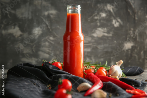 Bottle with tasty tomato sauce and vegetables on table