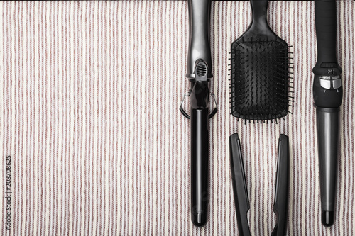 set of various hair straightening tools with metal plates and a comb on a grey striped background. concept of healthy care of hair. free space for text photo