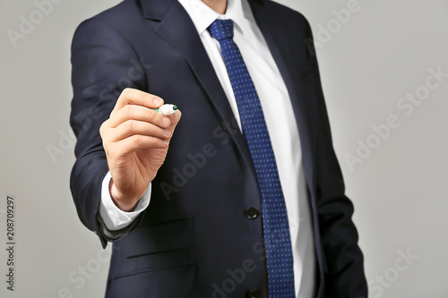 Young businessman writing on virtual screen against gray background