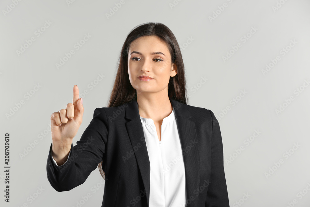 Young businesswoman using virtual screen on gray background Young businesswoman using virtual screen on gray background