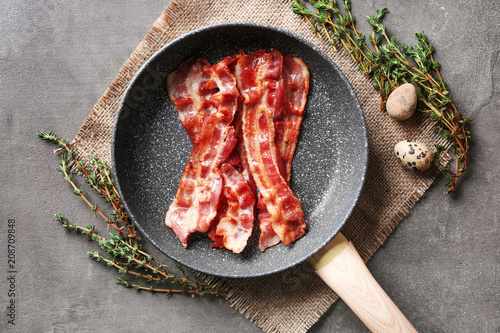 Frying pan with tasty bacon on grey background photo