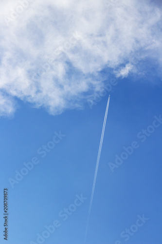 Skyscape with a plane with contrail approaching a fluffy cloud