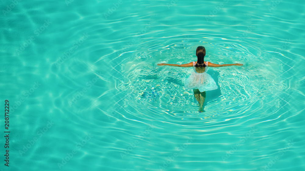 Girl in white dress in blue water pool on a clear sunny afternoon. Creative picture