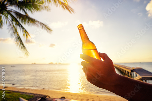 Fototapeta Naklejka Na Ścianę i Meble -  Vacation concept. Male hand holding bottle of beer on the sea beach.