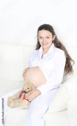 smiling pregnant woman sitting on sofa with teddy bear