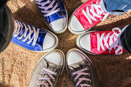 Red, blue and gray sneakers standing in the circle on dry sand, view from above . Friendship, fashion, lifestyle and adventure concept.