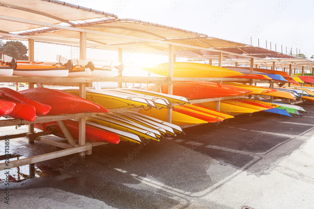 Fototapeta premium In sunlight, red, yellow and white kayaks placed upside down on metal storage racks. Stocked canoe in the Brest, France 28 May 2018