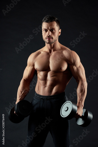 Attractive, handsome man holding heavy dumbbells. Athlete having strong, healthy, fit body with clear muscular relief and powerful hands. Looking sexy. Sport lifestyle. Feeling confident. © serhiibobyk