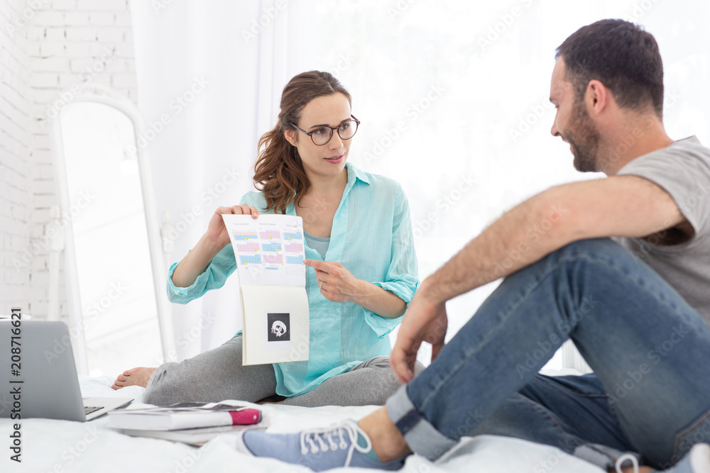 Fototapeta premium Monitor pregnancy. Beautiful pregnant woman and man talking while sitting on bed