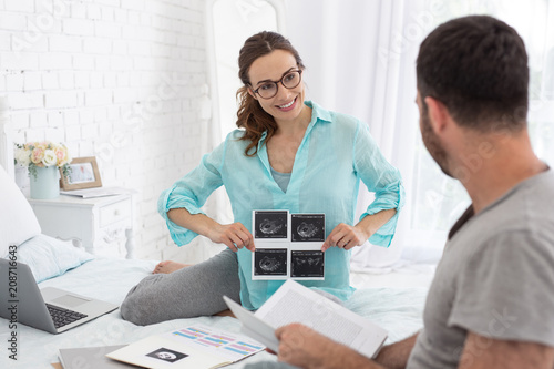 Baby in belly. Vigorous pregnant woman holding ultrasound while man looking at her
