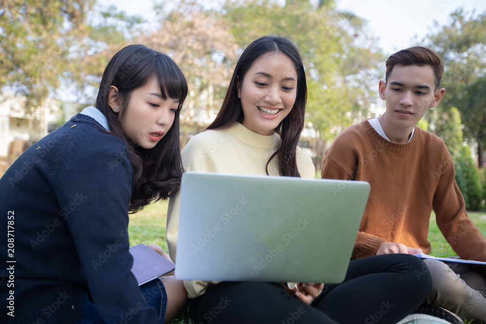 Group Of University Students asian sitting on the green grass Working and reading Outside Together in a park Group Of University Students asian sitting on the green grass Working and reading Outside Together in a park