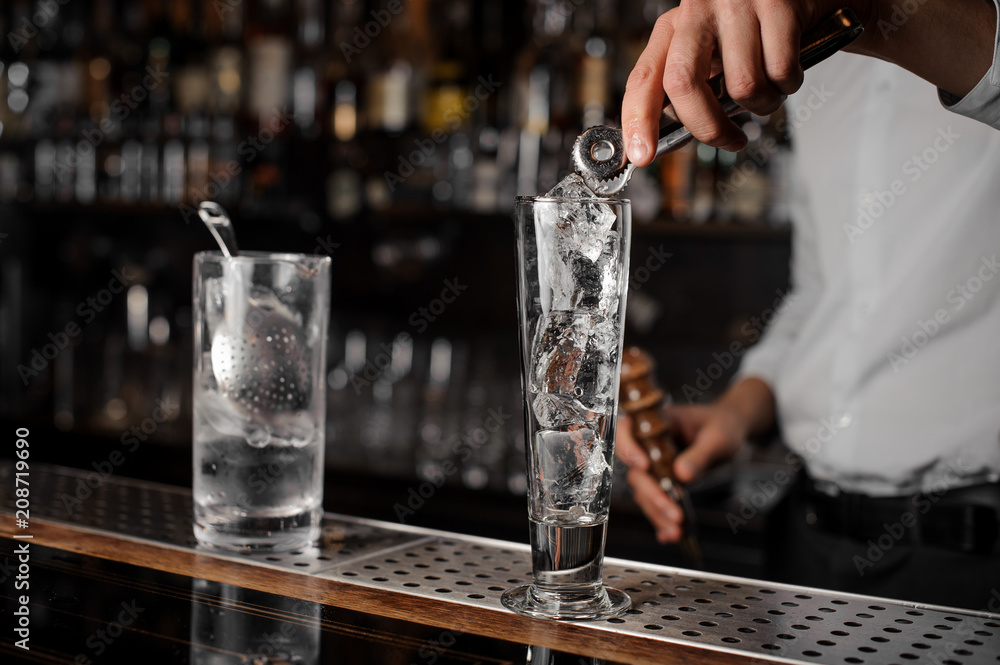 Bartender adding ice cubes into an empty cocktail glass