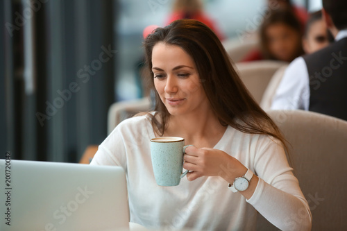 Young freelancer with cup of coffee and laptop working in cafe