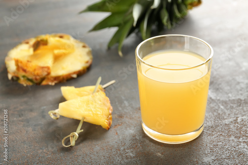 Glass of sweet juice with pineapple slices on table