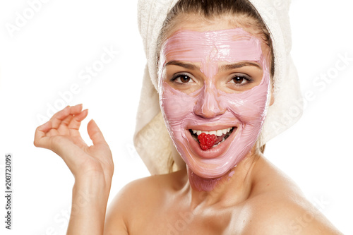 young smiling woman posing with  facial fruit  mask on her face , and with raspberry on her mouth