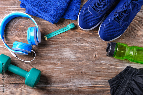 Flat lay composition with sneakers, headphones, dumbbell and bottle of water on wooden background. Gym workout