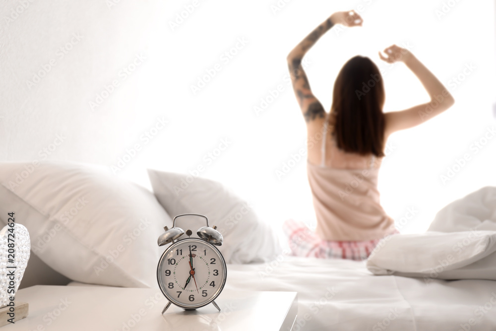 Table with alarm clock and young woman on bed in morning Table with alarm clock and young woman on bed in morning