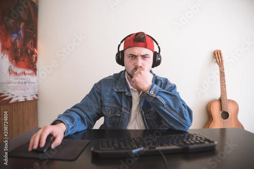 Serious man sits at the table and plays video games on a computer. Concentrated gamer plays games on the computer in a cozy room. Video Game Concept photo