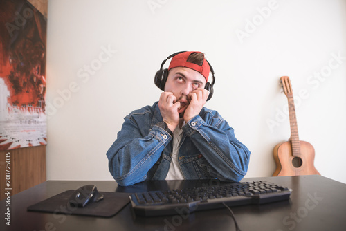 Funny man with a sad face sitting at the computer at headphones and playing video games. Portrait of a frustrating gamer for a home computer. photo