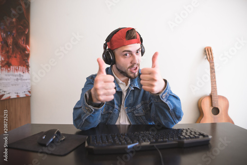 Adult gamer sits at home with a computer, shows a thumbs up and looks into the camera. A man sitting at home at the computer, playing video games and showing a thumbs up photo