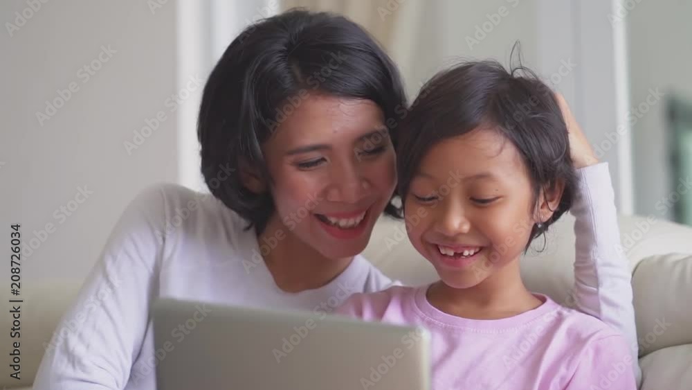 Cheerful mother and her daughter using a laptop computer while sitting on the couch at home Cheerful mother and her daughter using a laptop computer while sitting on the couch at home