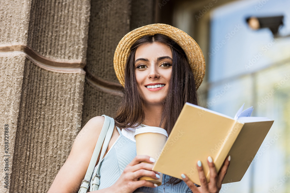 pretty smiling woman with opened book and coffee to go on street