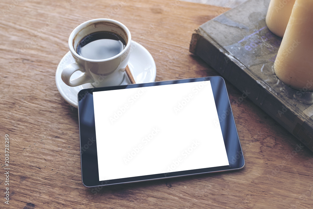 Top view mock up image of black tablet with white blank desktop screen and coffee cup , book , candles on vintage wooden table in cafe Top view mock up image of black tablet with white blank desktop screen and coffee cup , book , candles on vintage wooden table in cafe