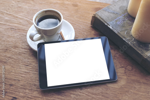 Fototapeta Naklejka Na Ścianę i Meble -  Top view mock up image of black tablet with white blank desktop screen and coffee cup , book , candles on vintage wooden table in cafe