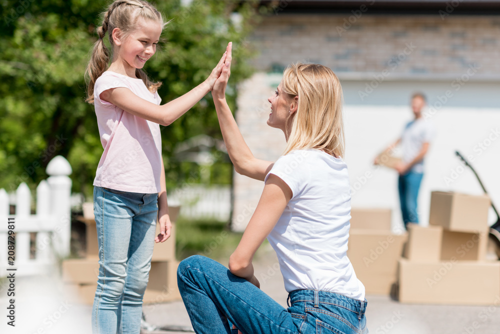 side view of mother taking high five to smiling daughter in front of new house
