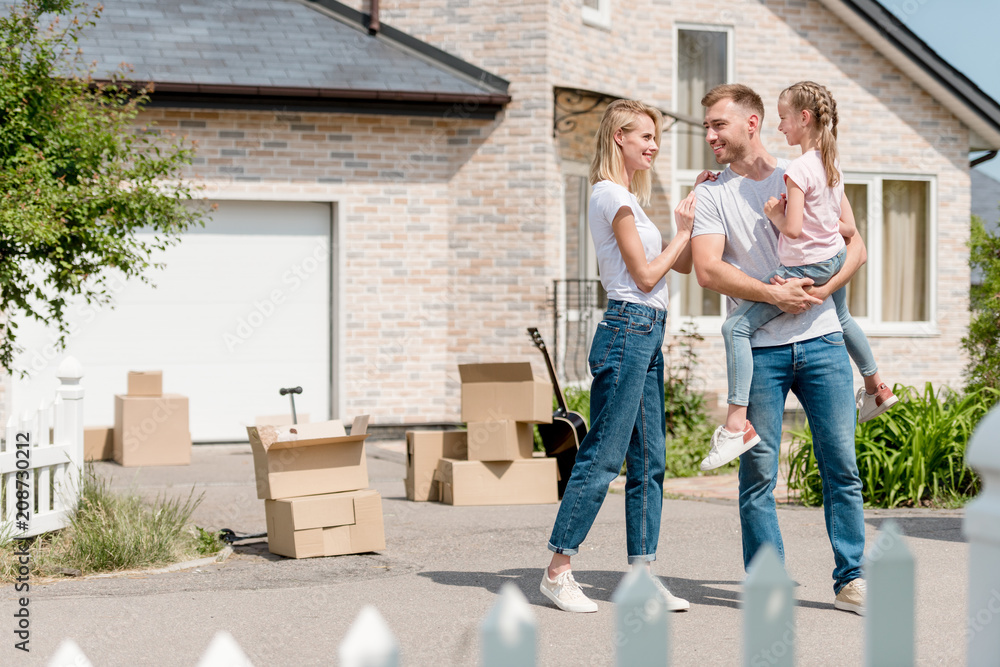 happy woman embracing smiling husband while he holding daughter inf front of new house happy woman embracing smiling husband while he holding daughter inf front of new house