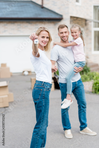 Woman showing key with trinket and her husband standing behind and holding daughter in front of their new cottage