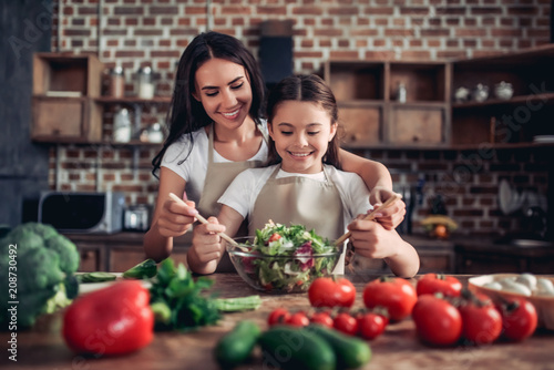 mother helping her daughter tossing the salad