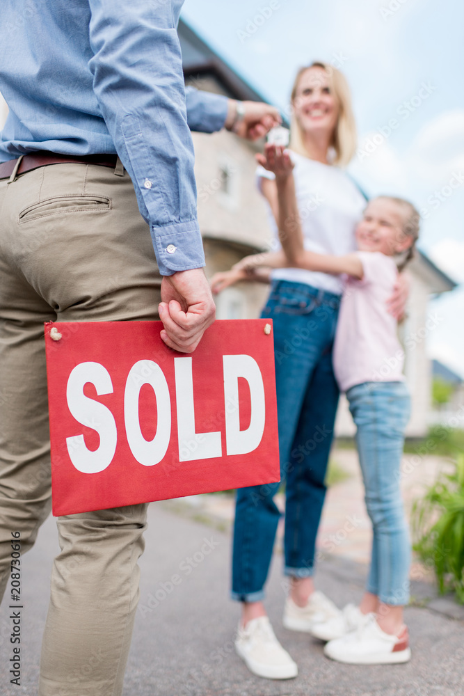cropped image of realtor with sold sign giving key to young woman with ...