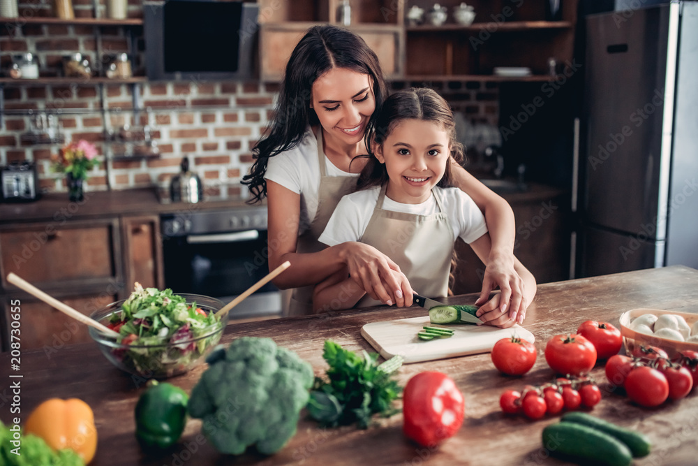 mother teaching her daughter to cut cucumber mother teaching her daughter to cut cucumber