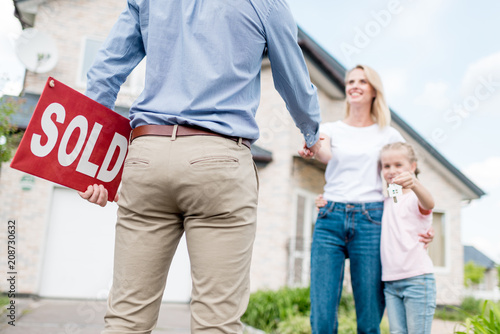 фотографія cropped shot of realtor with sold sign shaking hand of young woman with daughter
