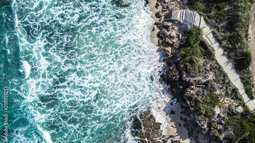 Aerial view ocean surf sea water washing onto sandy shoreline with stairs leading to beach