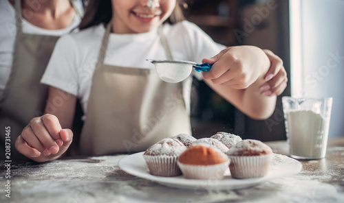 mother and daughter sprinkling with sugar powder cupcakes