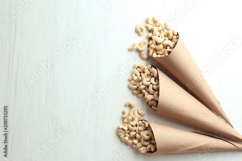 Paper cones with tasty cashew nuts on white wooden background
