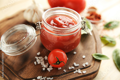 Delicious red sauce in glass jar on wooden board, closeup