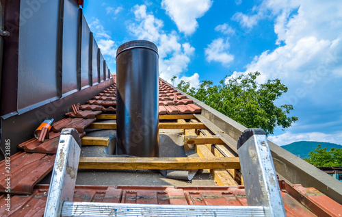Fotografia Installing external chimney trough a house roof with roof tiles.
