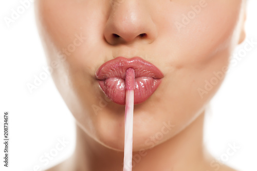 young beautiful woman apply a lip gloss on her lips on white background photo