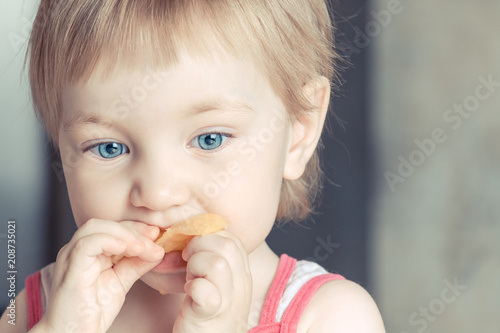 Sweet girl with big blue eyes eating orange slice.