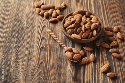 Bowl and spoon with almonds on wooden background
