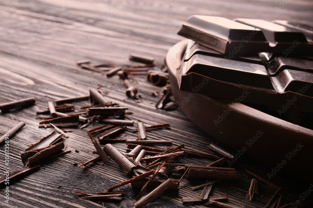 Plate with pieces of chocolate and curls on wooden table Plate with pieces of chocolate and curls on wooden table